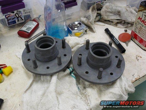 Two gray wheel hubs with five studs each, resting on white towels on a workbench