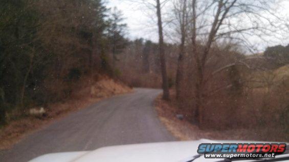 White vehicle hood and windshield wipers on a winding road through trees