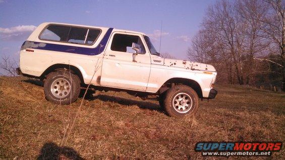 White and blue 1979 Ford Bronco parked on a grassy incline