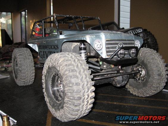 RC rock crawler with large tires and roll cage. Text on the side says 'ZEROFUCKS GIVEN'. Another vehicle is behind it