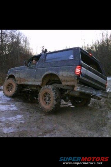 1995 Ford Bronco lifted and muddy driving on a dirt trail