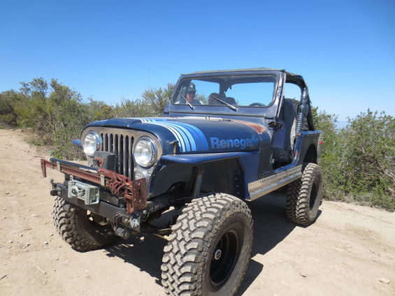 Blue Jeep CJ-7 Renegade with off-road tires and a winch, parked on a dirt road