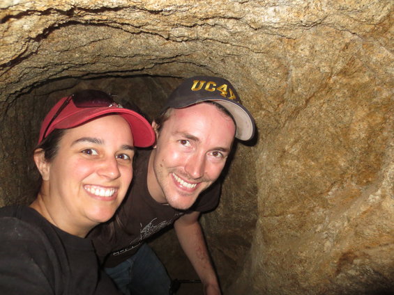 Two smiling people wearing hats inside a rocky cave