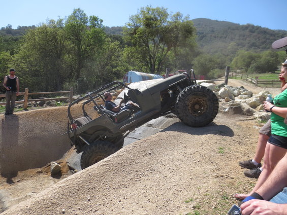Off-road buggy with roll cage climbing a dirt obstacle, driver visible