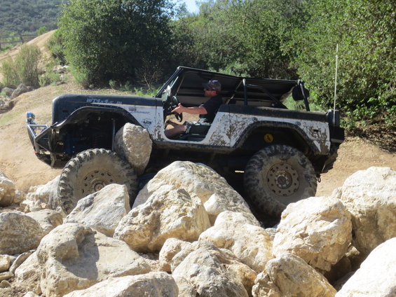 Mud-splattered black and white off-road vehicle with large tires navigating large rocks
