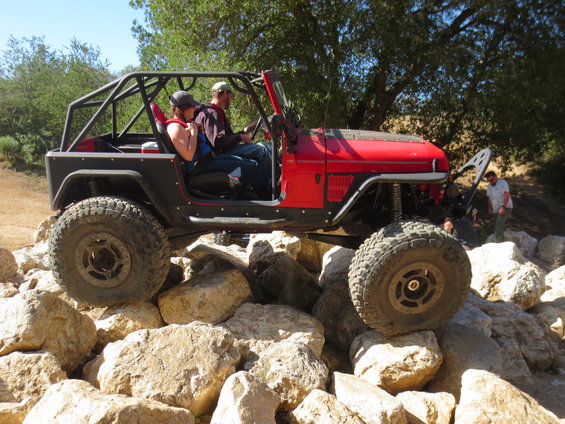 red Jeep with roll cage climbing over rocks, two people inside
