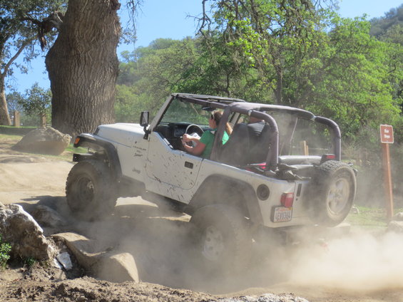 White Jeep Wrangler kicking up dust while driving over rocks on a dirt trail