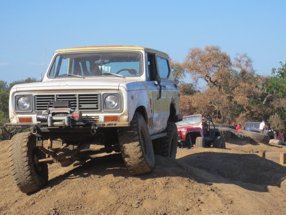 White International Harvester Scout II with yellow stripe, front winch, on dirt hill. Red Jeep and other off-road vehicles in background
