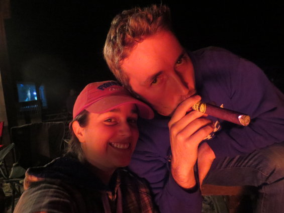 Woman in pink hat and man smoking cigar by campfire at night