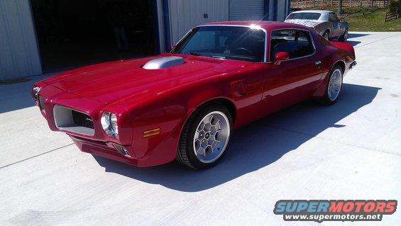 red coupe with hood scoop parked outside garage, another car in background