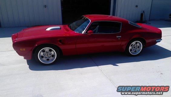 Red coupe with a silver hood scoop and distinctive wheels parked on a concrete surface