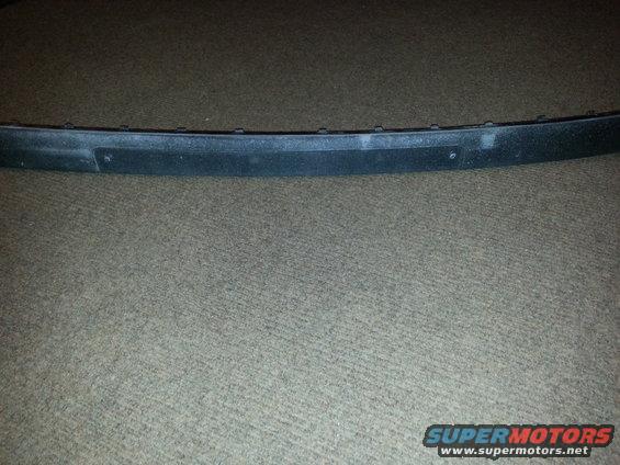 Black plastic trim piece with visible mounting holes, resting on carpet