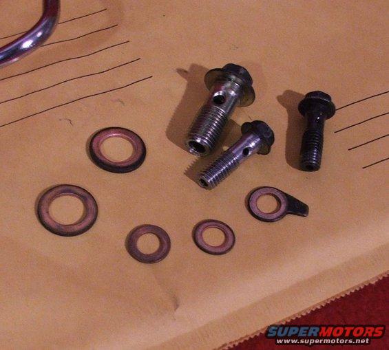 Banjo bolts and crush washers laid out on a brown surface with lines