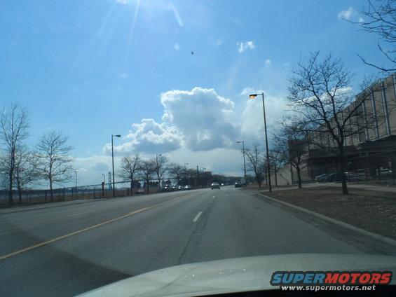 Driving down a road with cars and a large building on the right