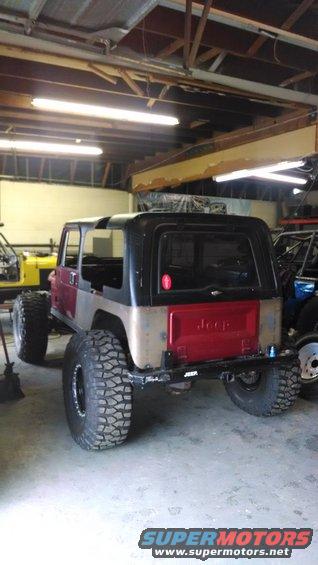 Jeep CJ-series with large tires, hardtop, and red tailgate. Body is partially painted