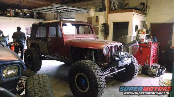 Red Jeep CJ-series with large tires, undergoing modification in a garage