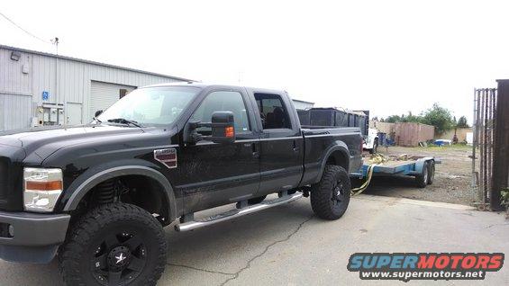 Black Ford F-350 Super Duty pickup truck with aftermarket wheels, towing a dual-axle trailer