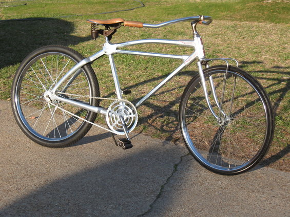Silver cruiser bicycle with leather seat and chrome handlebars, parked on a sidewalk