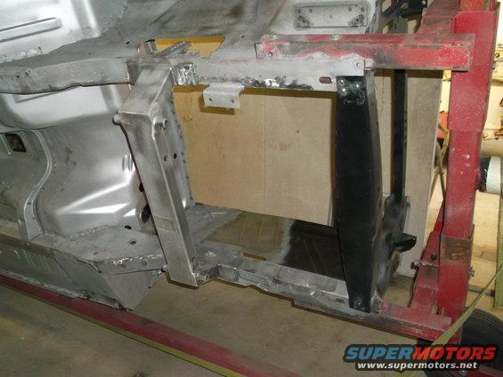Car frame section with metal bracing and wooden panel, viewed from the side