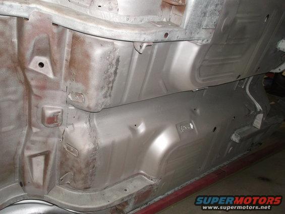 Underside of a car showing floor pans and frame rails, some rust visible