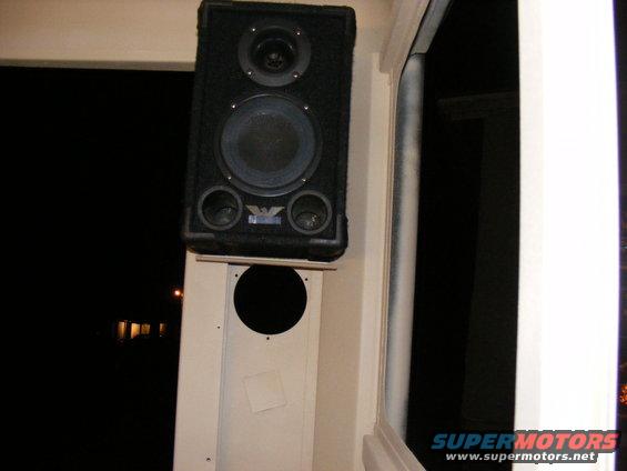 speaker mounted on a white panel, with a dark background outside