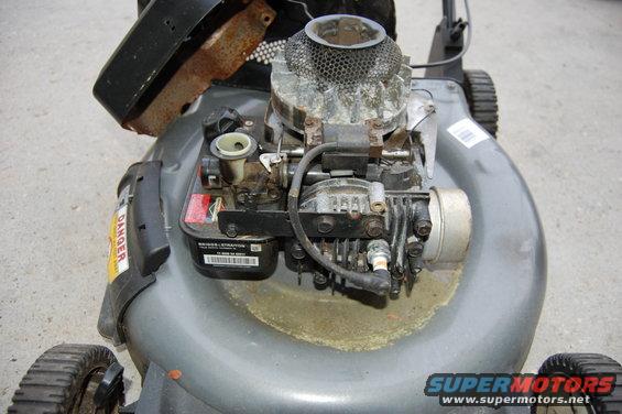 Gray lawn mower engine with rust and grass clippings, top view