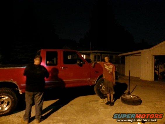 1995 Ford F-150 pickup truck, red, with two men standing next to it at night