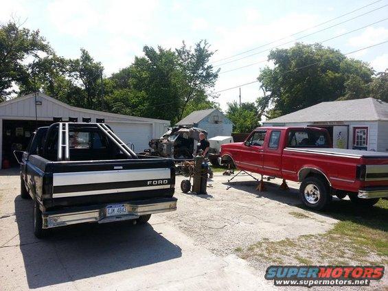 Black Ford truck in foreground, red Ford truck on jacks in background. Someone is welding