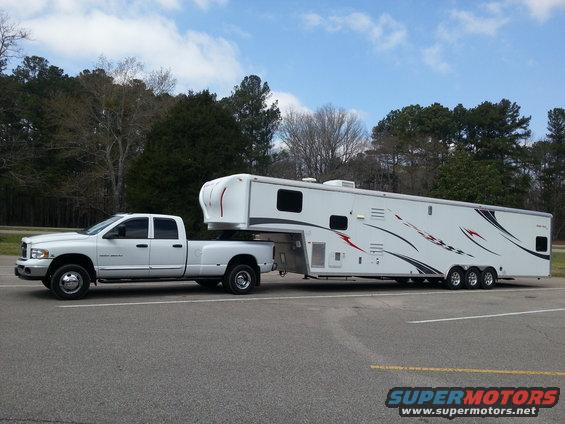White Dodge Ram 3500 dually pickup truck towing a large white fifth-wheel trailer with red and black graphics