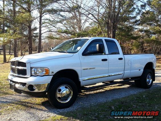 White Dodge Ram 3500 dually pickup truck parked on a gravel surface with trees in the background