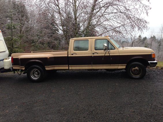 Side view of a two-tone brown and tan Ford F-350 crew cab pickup truck towing a small trailer