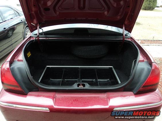 Trunk interior of a 2004 Mercury Grand Marquis showing spare tire and organizer tray. Another car is visible to the left