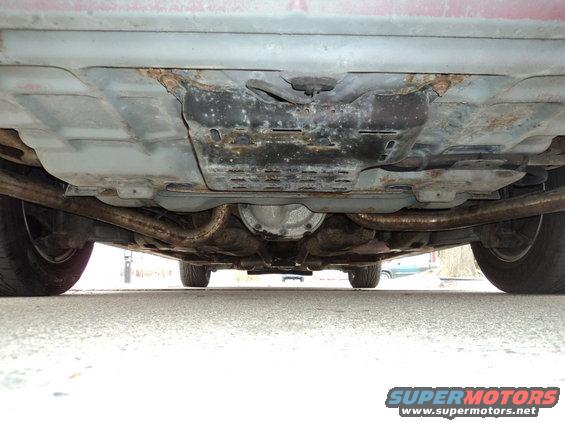 Underside of a red 2004 Mercury Grand Marquis showing rusted exhaust pipes and differential