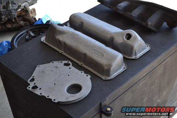 Two Ford valve covers and a timing cover on a black surface. Supermotors.net logo visible