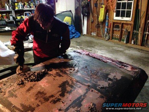 guy scraping rust off a car hood in a garage