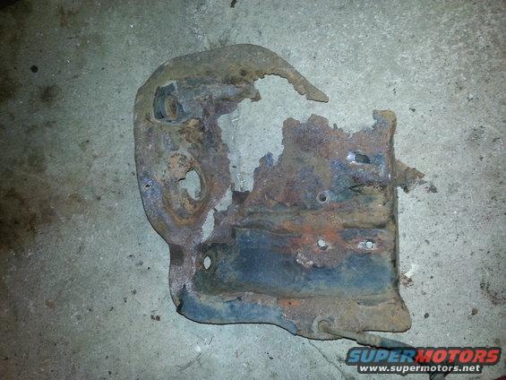 Heavily rusted and damaged metal bracket with holes and torn edges, lying on a concrete surface