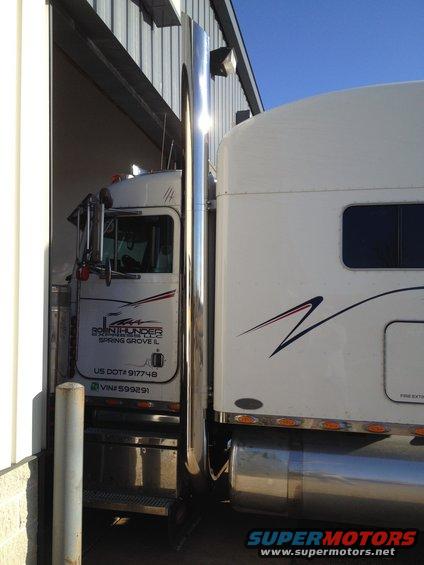 Semi-truck cab with 'BRINTHUNDER' logo and trailer parked next to a building