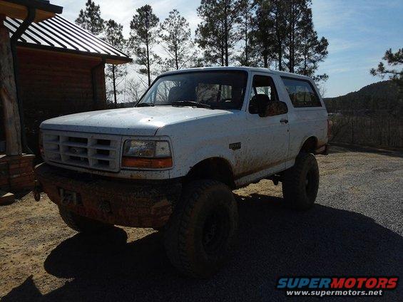 1995 Ford Bronco with lifted suspension and aftermarket front bumper, parked near a wooden building