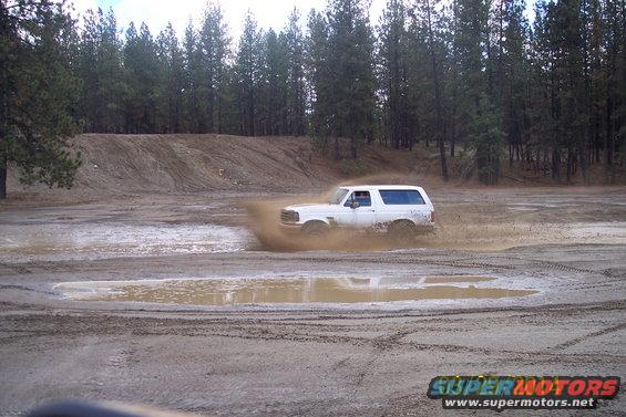 White 1990 Ford Bronco splashing mud while driving off-road