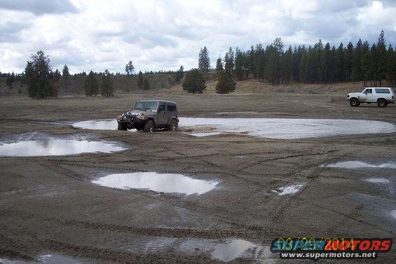 White SUV driving through a muddy field with a Jeep in the foreground