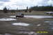 1990 Ford Bronco - A white SUV navigates a muddy terrain, with a Jeep visible in the foreground puddle.