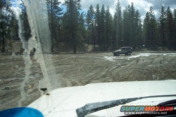 SUV driving on dirt road near pine trees, seen from inside another vehicle