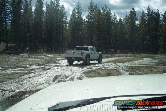 White pickup truck rear view on muddy terrain with another vehicle in the distance
