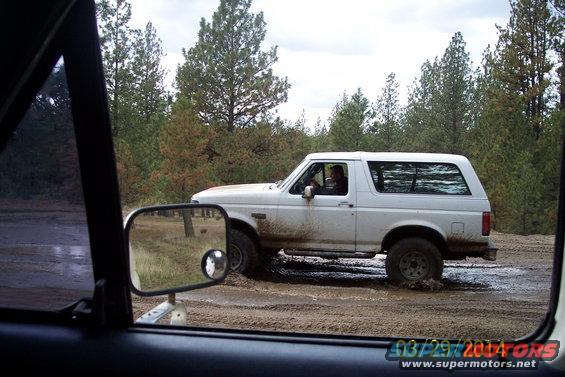 White 1990 Ford Bronco driving through mud, side view