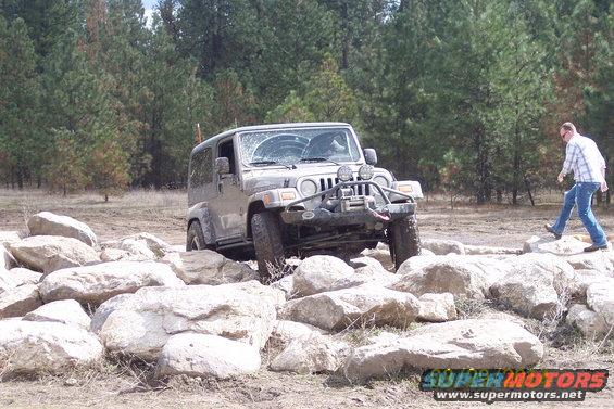 Jeep Wrangler navigating a rocky trail with a person walking nearby