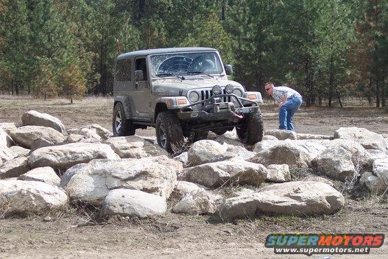 Gray Jeep Wrangler TJ with winch and brush guard on rocky terrain