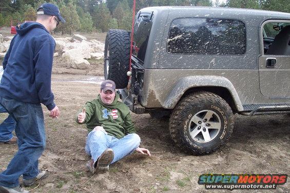 Mud-splattered Jeep Wrangler with a spare tire mounted on the rear, seen from the back