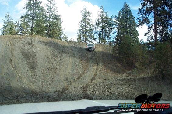 White SUV climbing a steep dirt incline, seen from inside another vehicle
