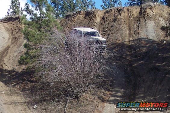 white SUV driving up a dirt hill, trees and bushes around