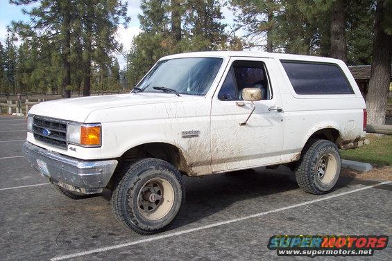 White Ford Bronco with mud splatters, parked in a lot